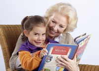 Eine ältere Dame sitzt zusammen mit ihrer Enkelin und liest in einem Buch.