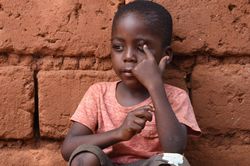 Ein Kind sitzt an eine Mauer gelehnt und hält sich ein Auge zu.
