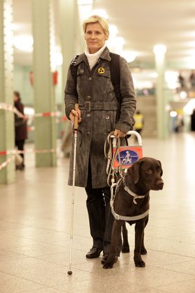 Eine blinde Frau läuft mit ihrem Blindenführhund in einer U-Bahnstation.