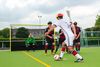 Spielszene im Blindenfußball. Ein Spieler mit weißen Trikot umläuft mit dem Ball drei Spieler in schwarz-roten Trikots. Im Hintergrund ist das Tor mit Torhüter zu sehen.