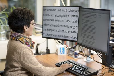 Eine weibliche Person sitzt vor zwei Bildschirmen. Einer der Bildschirme stellt den Inhalt des anderen stark vergrößert dar.