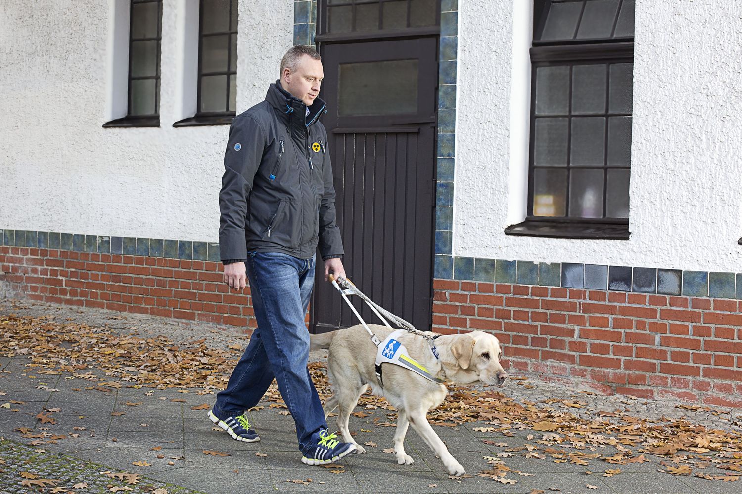 Ein Mann mit Führhund läuft einen Gehweg entlang.