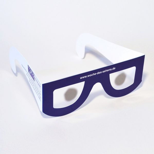 Simulationsbrille Altersabhängige Makula-Degeneration (AMD), eine Brille mit „Gläsern“ aus Folie, breiten Bügeln aus weißer Pappe und Fassung aus dunkelblauer Pappe, die Brillenfolie ist in der Mitte undurchsichtig-hellgrau.