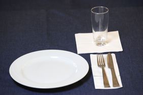 Beispiele für Kontraste: Weißer Teller auf blauer Tischdecke, unter einem Glas und dem Essensbesteck ist jeweils eine weiße Serviette platziert, die sich von der blauen Tischdecke abhebt.