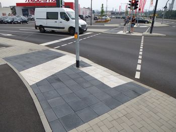 Nahaufnahme eines Gehweges an einer Straßenkreuzung. Ein Noppenfeld dient als Auffindestreifen zum Bereich der Querung für blinde und sehbehinderte Menschen