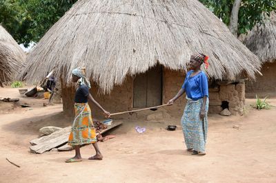 Ein Mädchen in einem afrikanischen Dorf führt eine ältere Frau am Stock hinter sich.