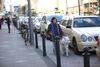 Eine Frau läuft mit ihrem Blindführhund an geparkten Taxis entlang