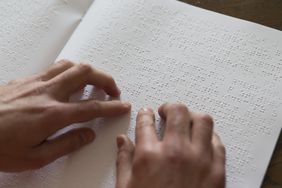 Blick auf zwei Hände auf einer Buchseite mit Brailleschrift