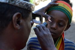 Ein Augenarzt eines Entwicklungslandes untersucht die Augen eines Kindes und Leute mit einer Lampe in sein Auge.