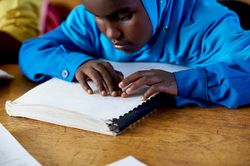 Kinderblindheit – Lesen mit Brailleschrift Ein blindes Mädchen liest in einem Heft mit Brailleschrift.