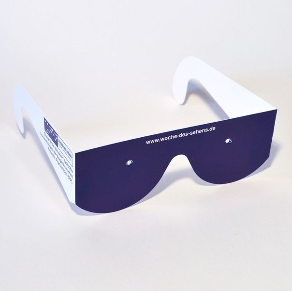 Simulationsbrille Retinits Pigmentosa, eine Brille mit breiten Bügeln aus weißer Pappe und Fassung und „Gläsern“ aus dunkelblauer Pappe, ein kleines Loch in der Mitte des dunkelblauen „Glases“.