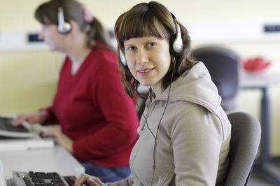 Zwei weibliche Personen sitzen mit Kopfhörern und Braillezeile am Computer.