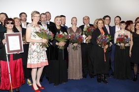 Die Preisträger und Jury-Mitglieder stehen in einer Reihe, der Kamera zugewandt, vor einer weißen Wand.