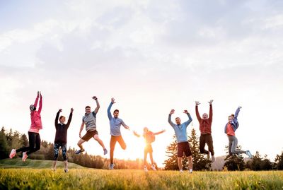 8 Jugendliche hüpfen auf einer Wiese, im Hintergrund Hügel und eine tief stehende Sonne.