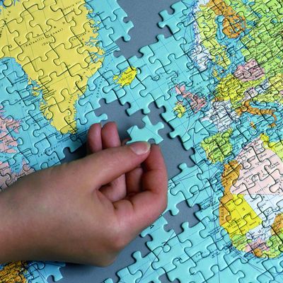 In ein Puzzle einer Weltkarte, von der ein Ausschnitt gezeigt wird, fügt eine Hand ein weiteres Puzzleteil ein. Das Bild ist scharf, die Bildelemente sind gut erkennbar.
