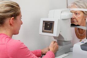 Eine Arzthelferin vermisst mit Hilfe eines Gerätes berührungsfrei das Auge einer älteren Patientin.